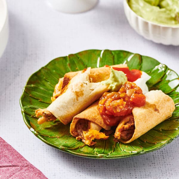 Vegetarian flautas on green plate with salsa and guacamole.