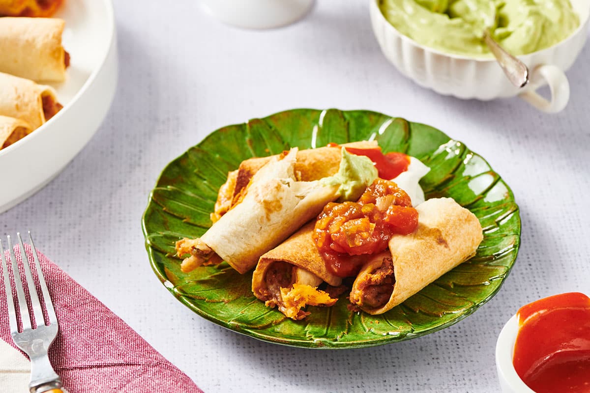 Vegetarian flautas on green plate with salsa and guacamole.