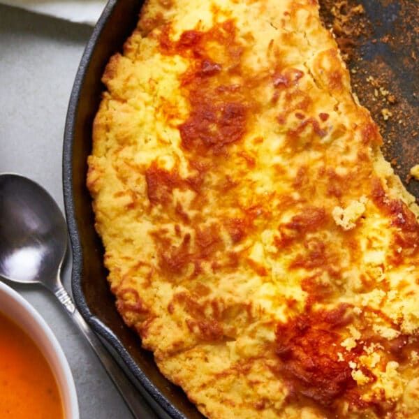 Cheddar cornbread in cast iron skillet next to bowls of tomato soup.