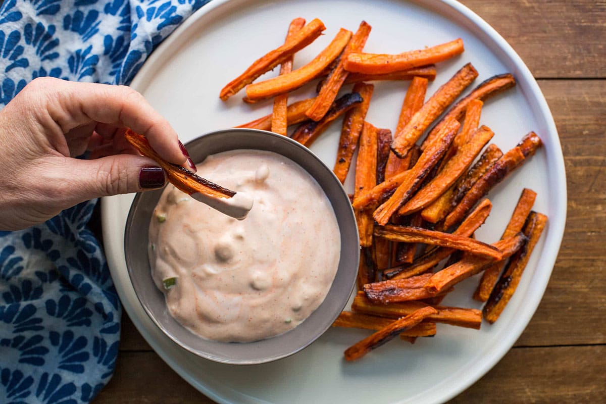 Woman dipping carrot fries into bowl of Sriracha sauce.