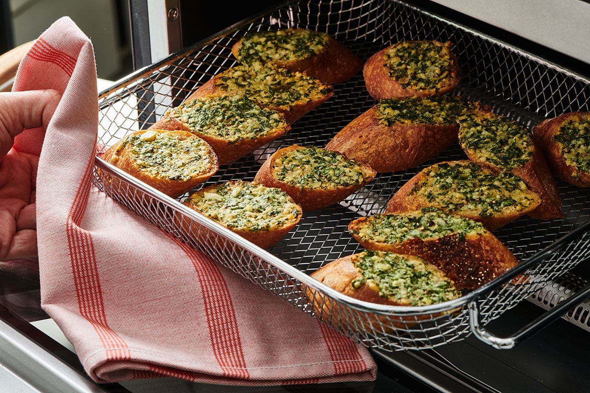 Removing air fryer tray with garlic bread with towel.