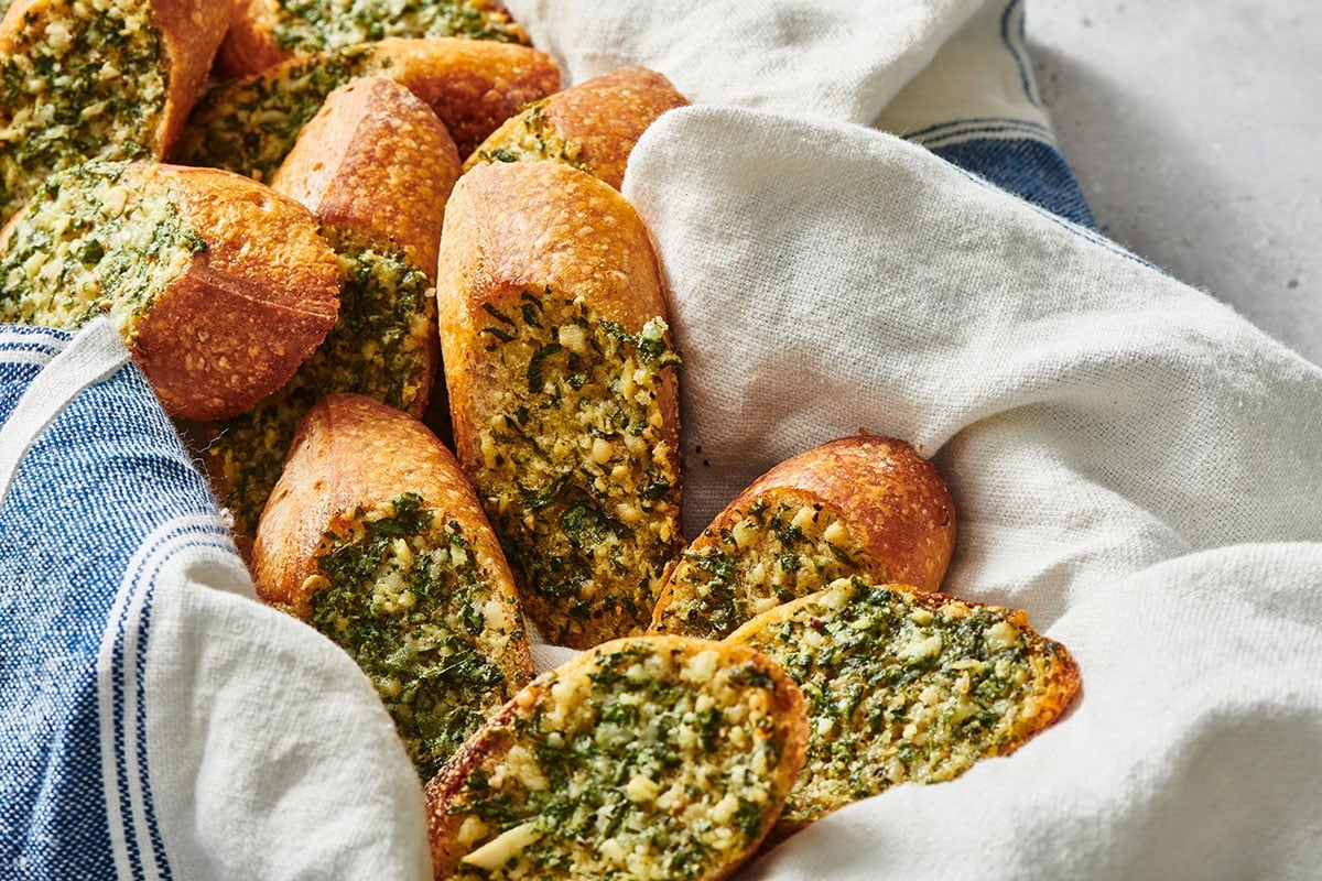 Air fryer garlic bread slices smothered in herb garlic butter in towel-lined basket.