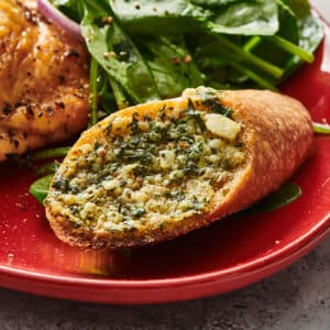 Air-fried garlic bread on red plate with salad and chicken.