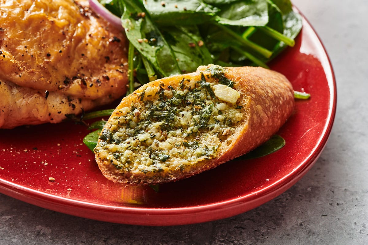 Air-fried garlic bread on red plate with salad and chicken.