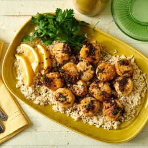 Seared sea scallops in lemon butter sauce over rice with lemon and parsley on yellow plate.