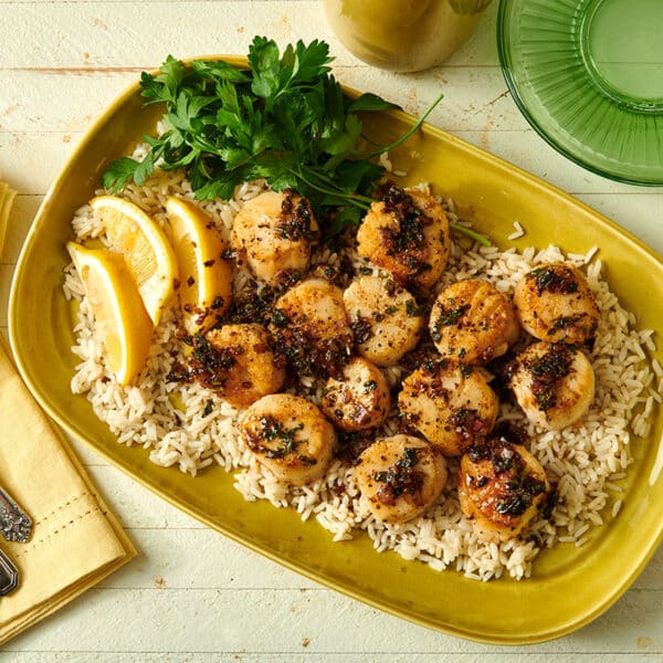 Seared sea scallops in lemon butter sauce over rice with lemon and parsley on yellow plate.