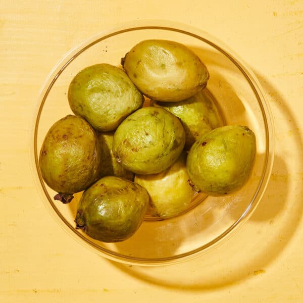 Whole guava in glass bowl on yellow table.