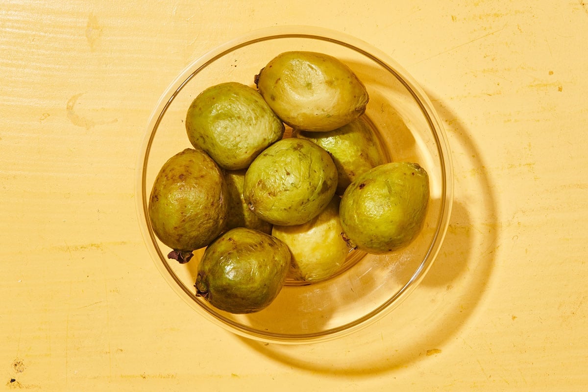 Whole guava in glass bowl on yellow table.