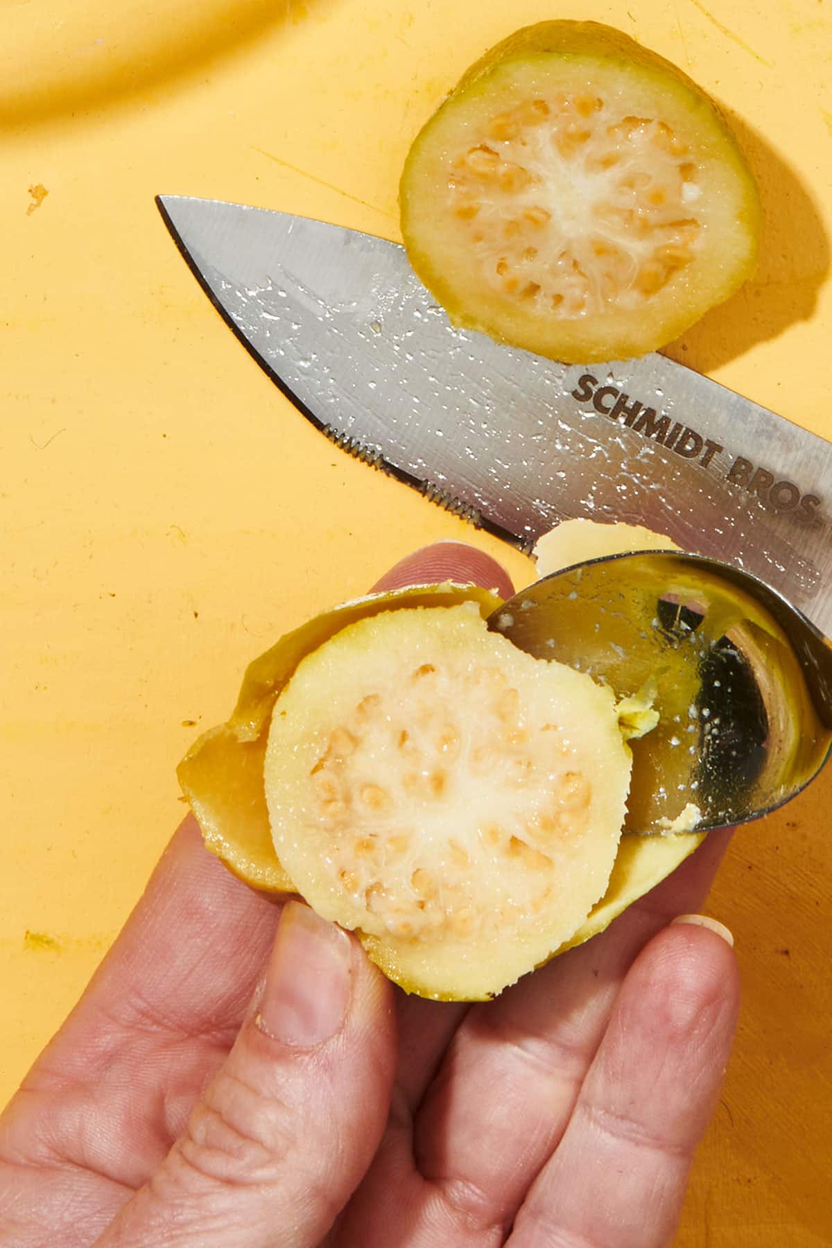 Scooping fresh guava pulp out of rind with spoon.