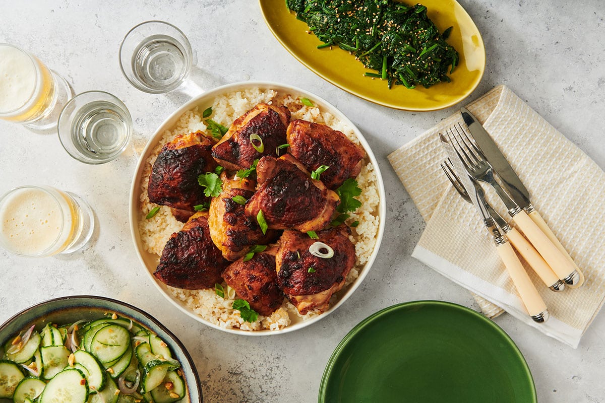 Miso chicken on plate over rice with salads, drinks, and silverware on tables