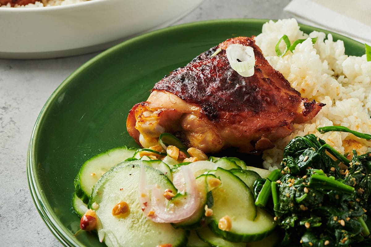 Baked miso-flavored chicken thigh on green plate with rice and salads.