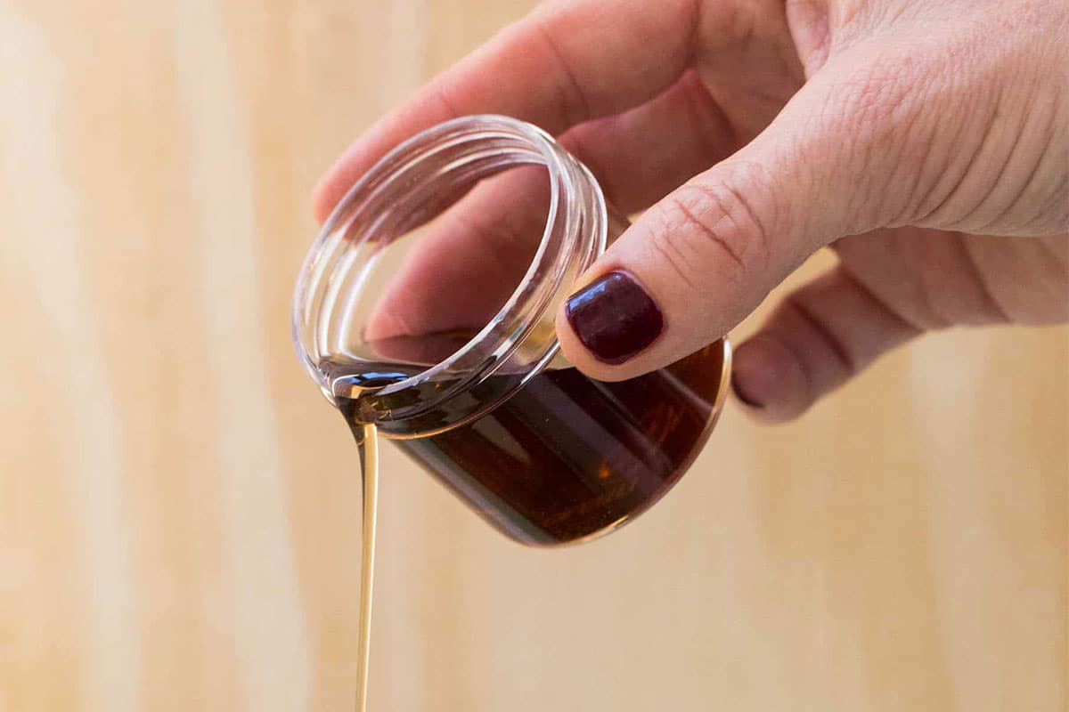 Woman pouring maple syrup from small glass jar.
