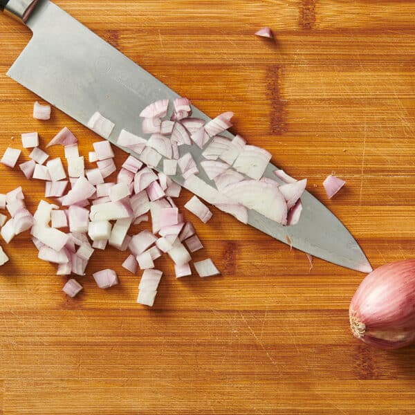 Chopped and whole shallots on wood cutting board with knife.