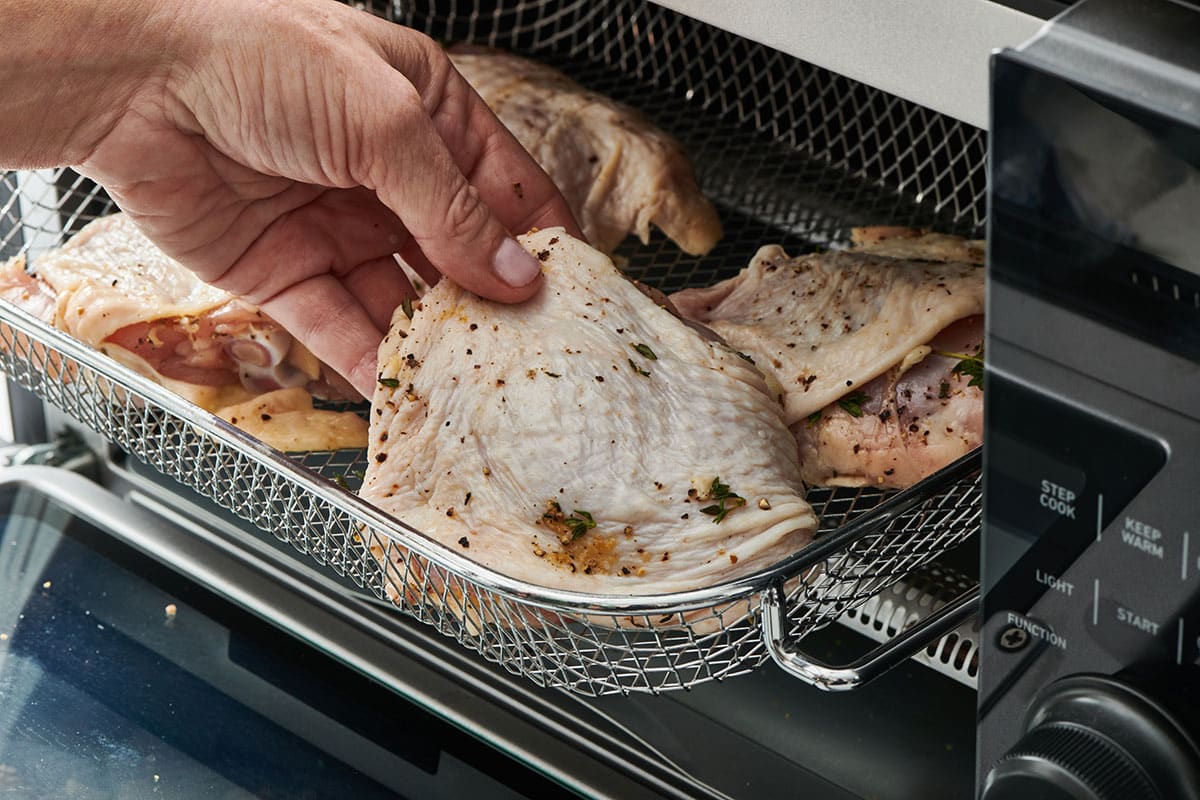 Katie Workman placing raw chicken thighs in air fryer basket.