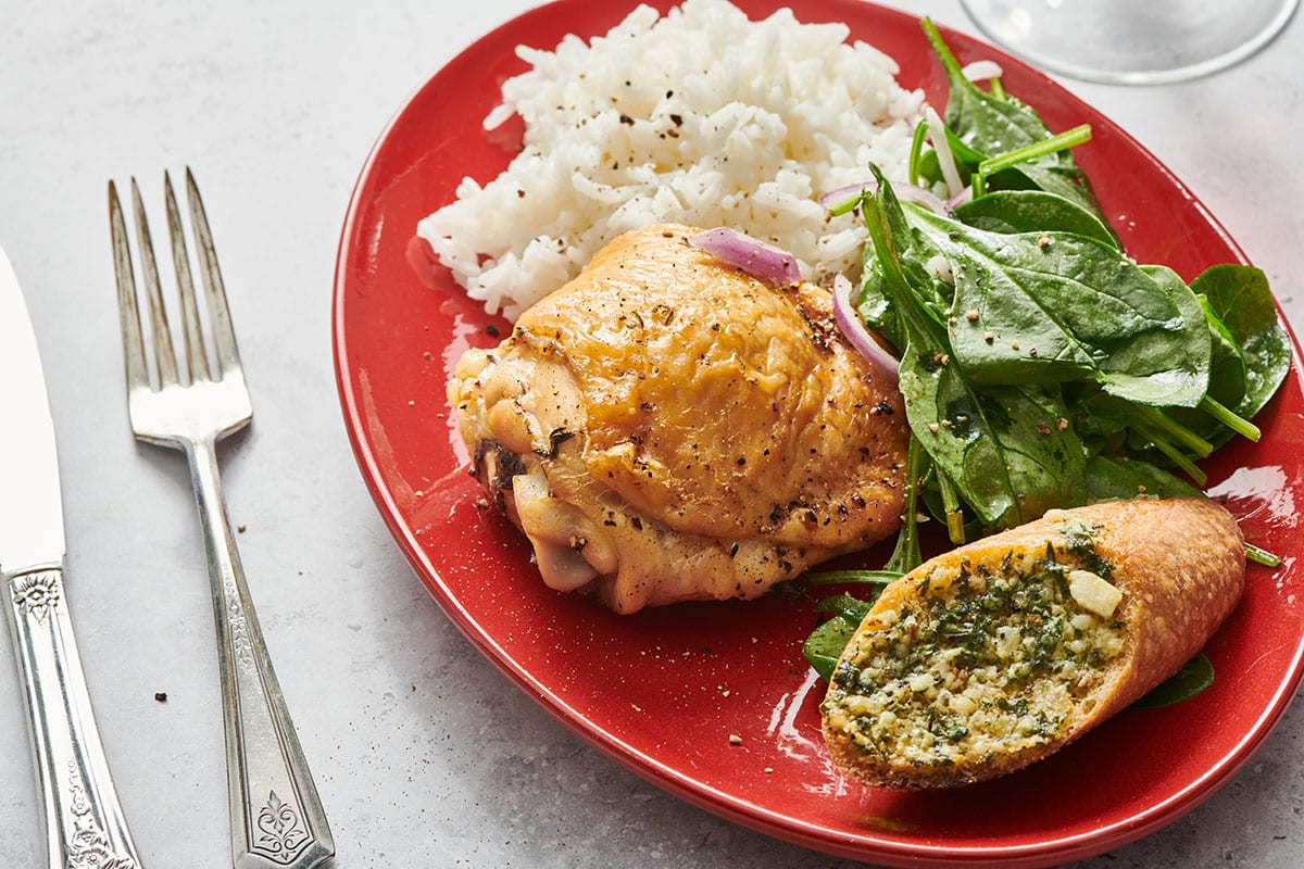 Air-fried chicken thigh on red plate with rice, salad, and garlic bread.