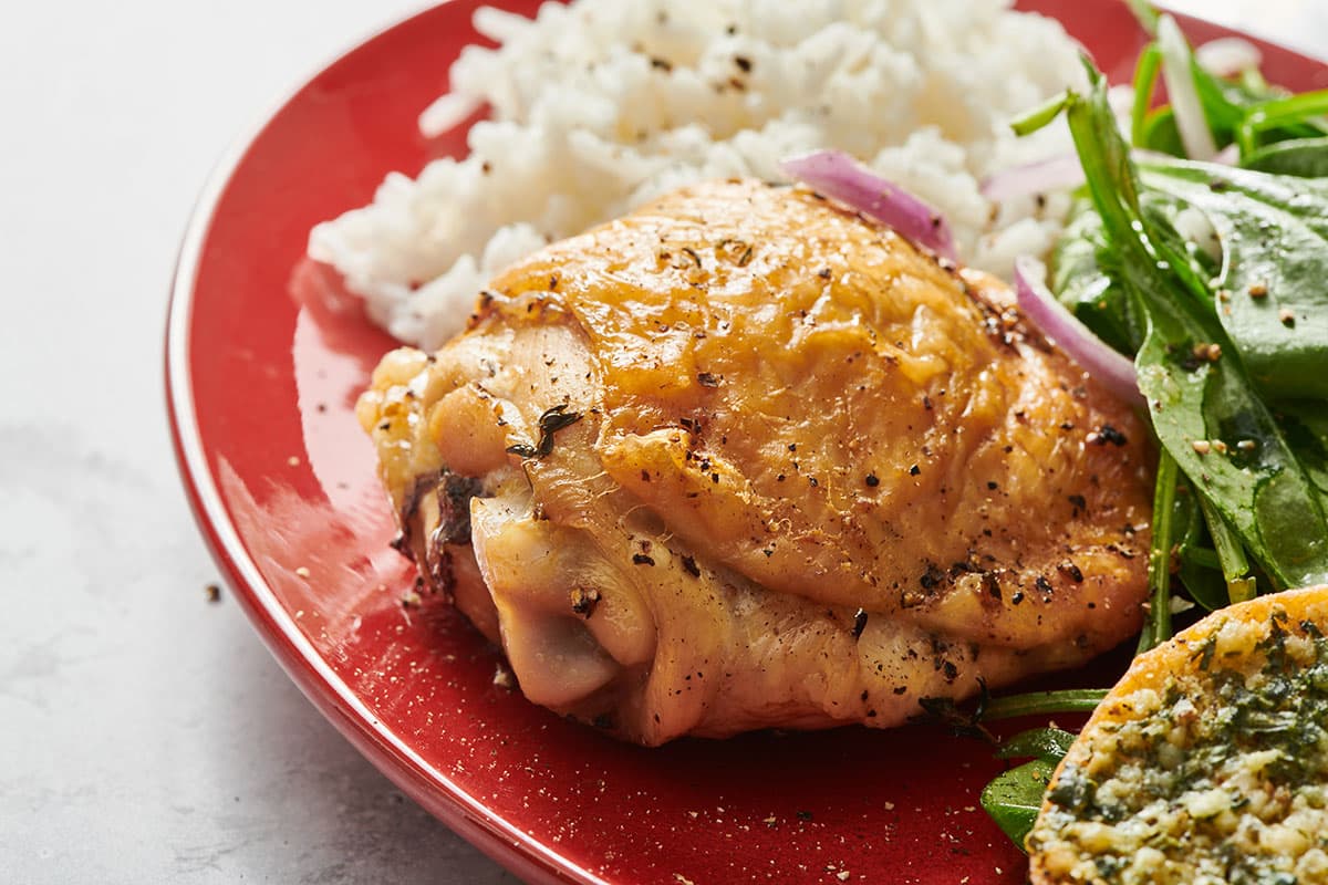 Air-fried chicken thigh on plate with rice, salad, and other side dishes.