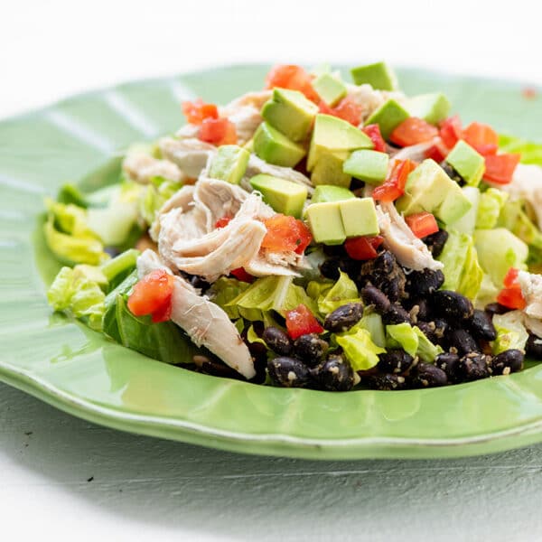 Tostada with chicken, black beans, lime cilantro crema and toppings on green plate.