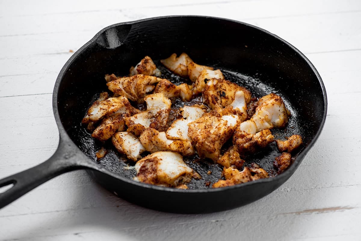 Pieces of fried white fish in cast iron pan.