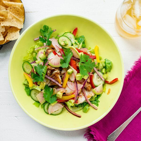 Fish taco bowl in yellow bowl on table with tortilla chips and drink.