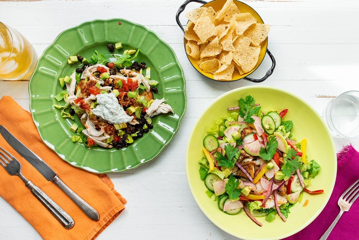 Fish taco bowls in green and yellow bowl with toppings on table with tortilla chips.
