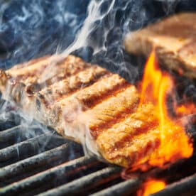 Salmon fillets on hot grill with flames.