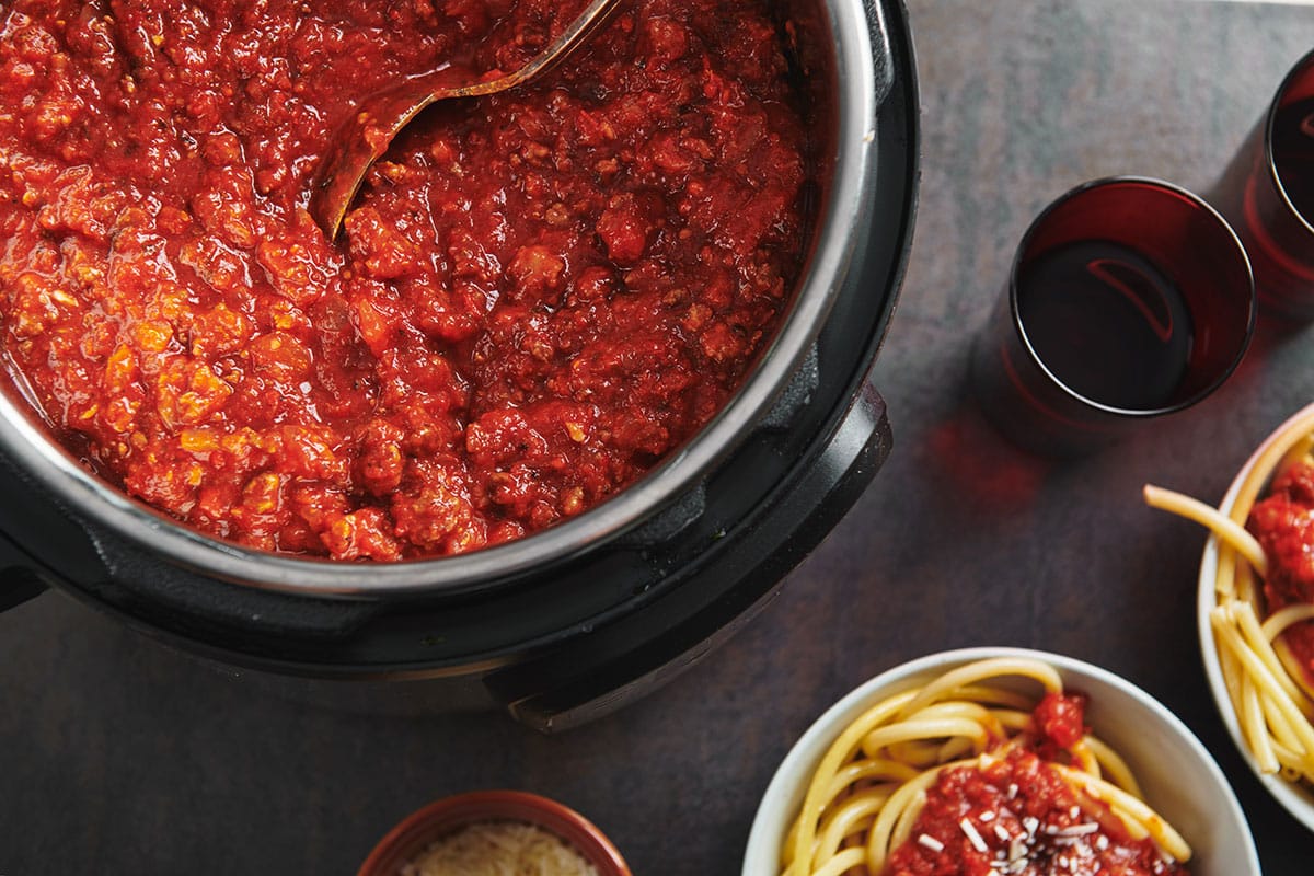 Meat sauce in Instant Pot and in bowls over spaghetti.