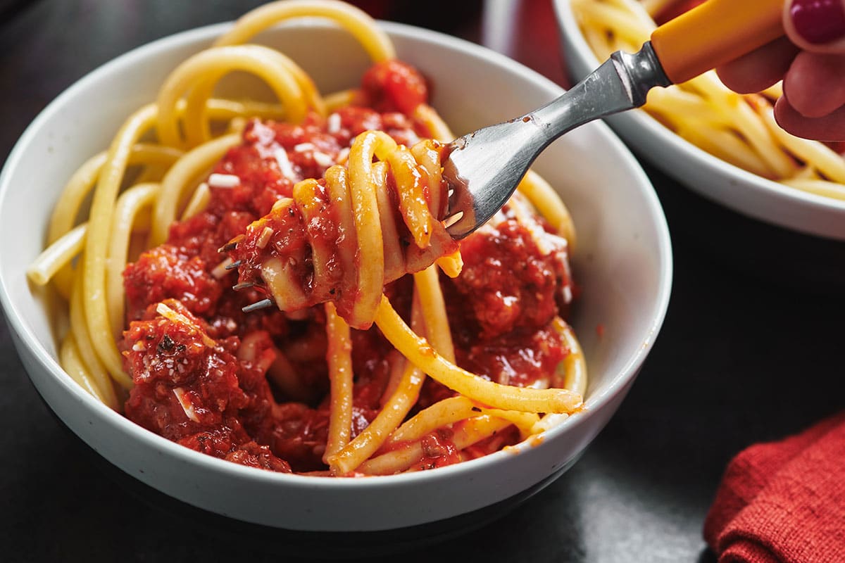 Fork grabbing spaghetti and meat sauce in white bowl.