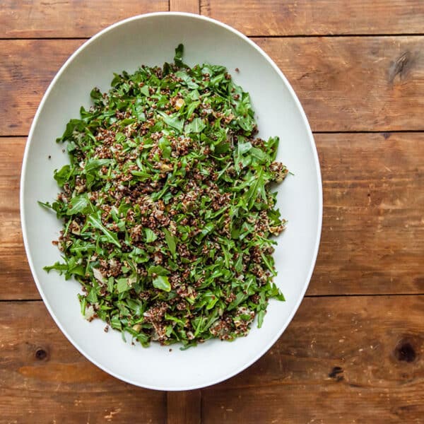 White bowl on table filled with salad of red quinoa, arugula, and artichoke hearts.
