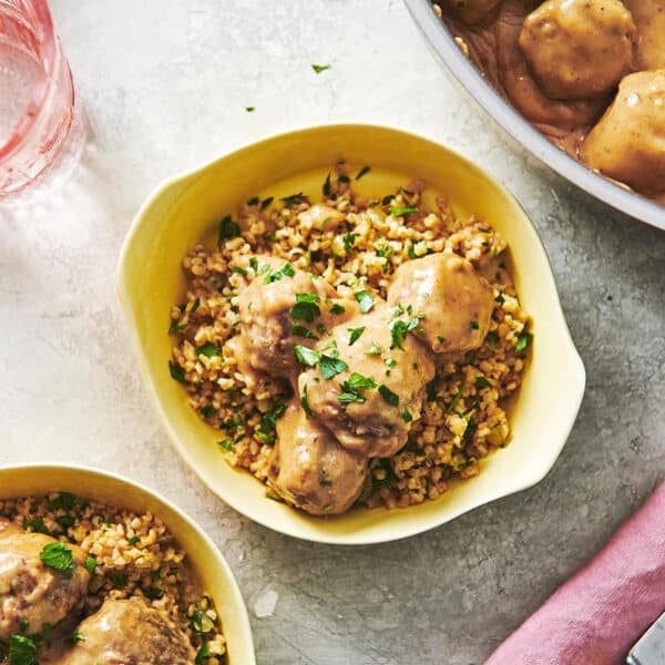 Swedish Meatballs in yellow bowls with fresh herbs on table.