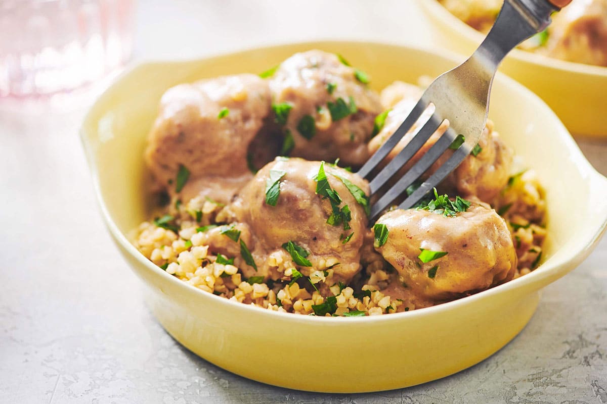 Fork grabbing Swedish meatballs from yellow bowl.