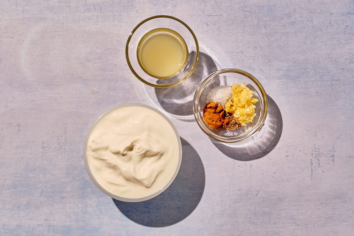 Yogurt, garlic, lemon zest, and other sauce ingredients in small bowls on table.