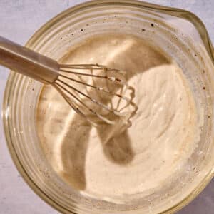 Homemade Mediterranean-style garlic yogurt sauce in glass bowl with whisk.