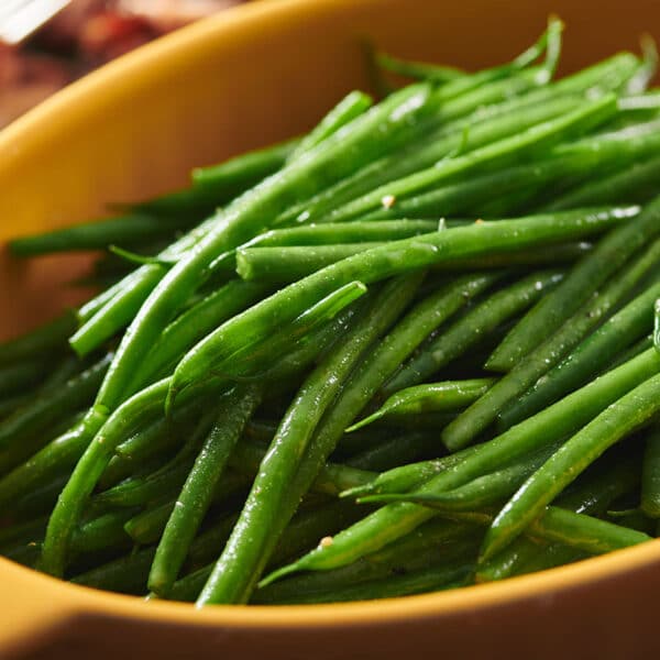 Blanched green beans in large yellow serving dish on table.