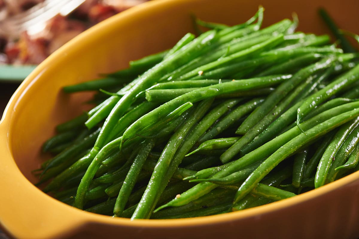 Blanched green beans in large yellow serving dish on table.