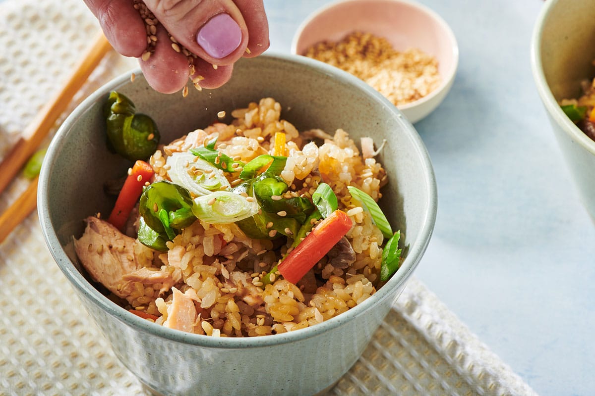 Garnishing bowl of salmon takikomi with matsuba leaves and toasted sesame seeds.