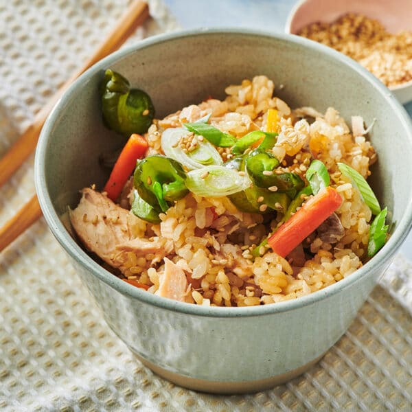 Salmon takikomi gohan in grey bowls with vegetable garnishes on table with chopsticks and drinks.