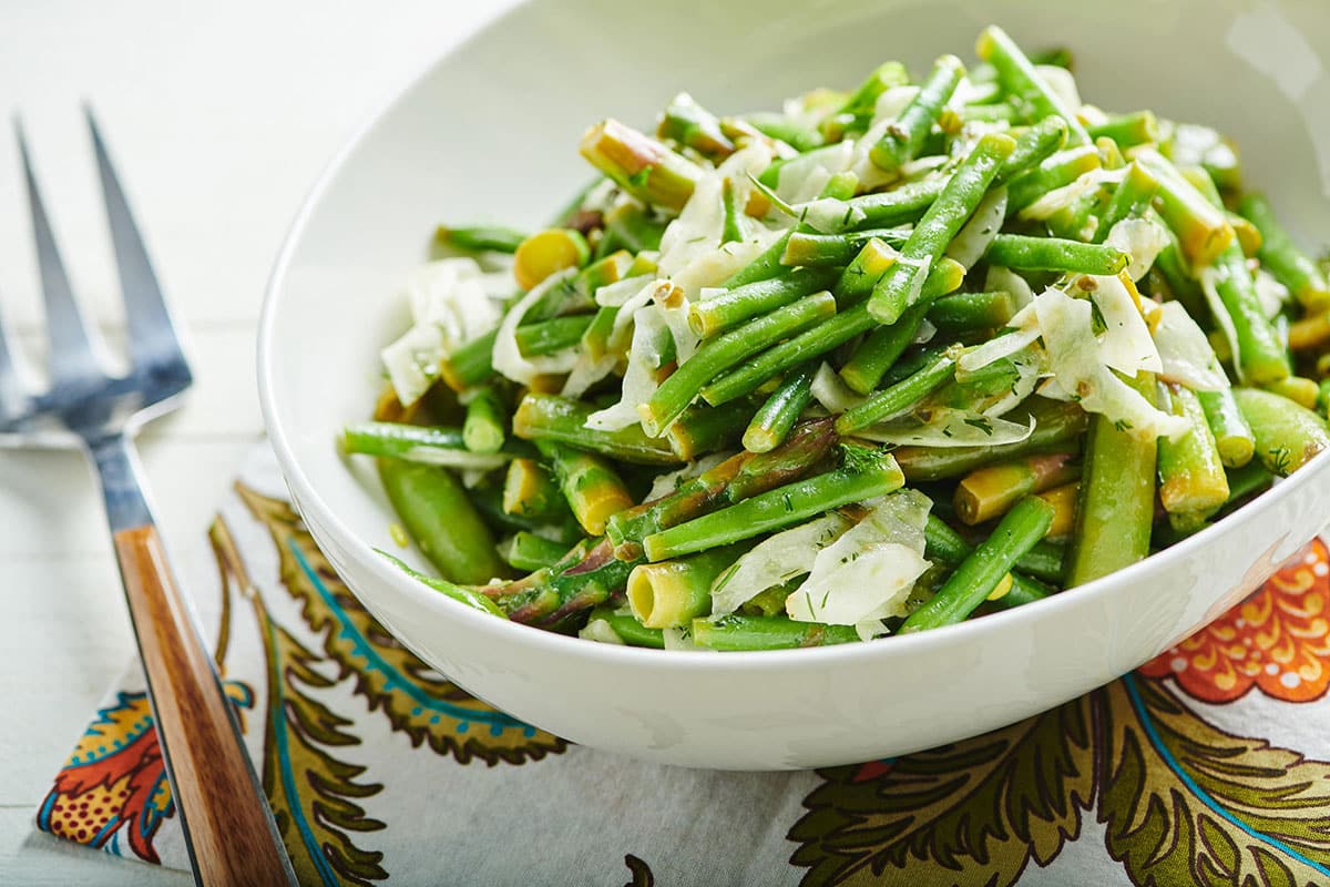 Sprig vegetable salad with blanched green beans in large white bowl.