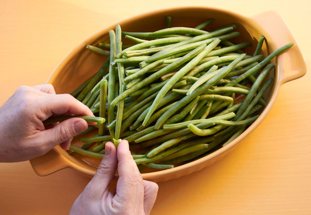 Katie Workman trimming fresh green beans over large yellow bowl.