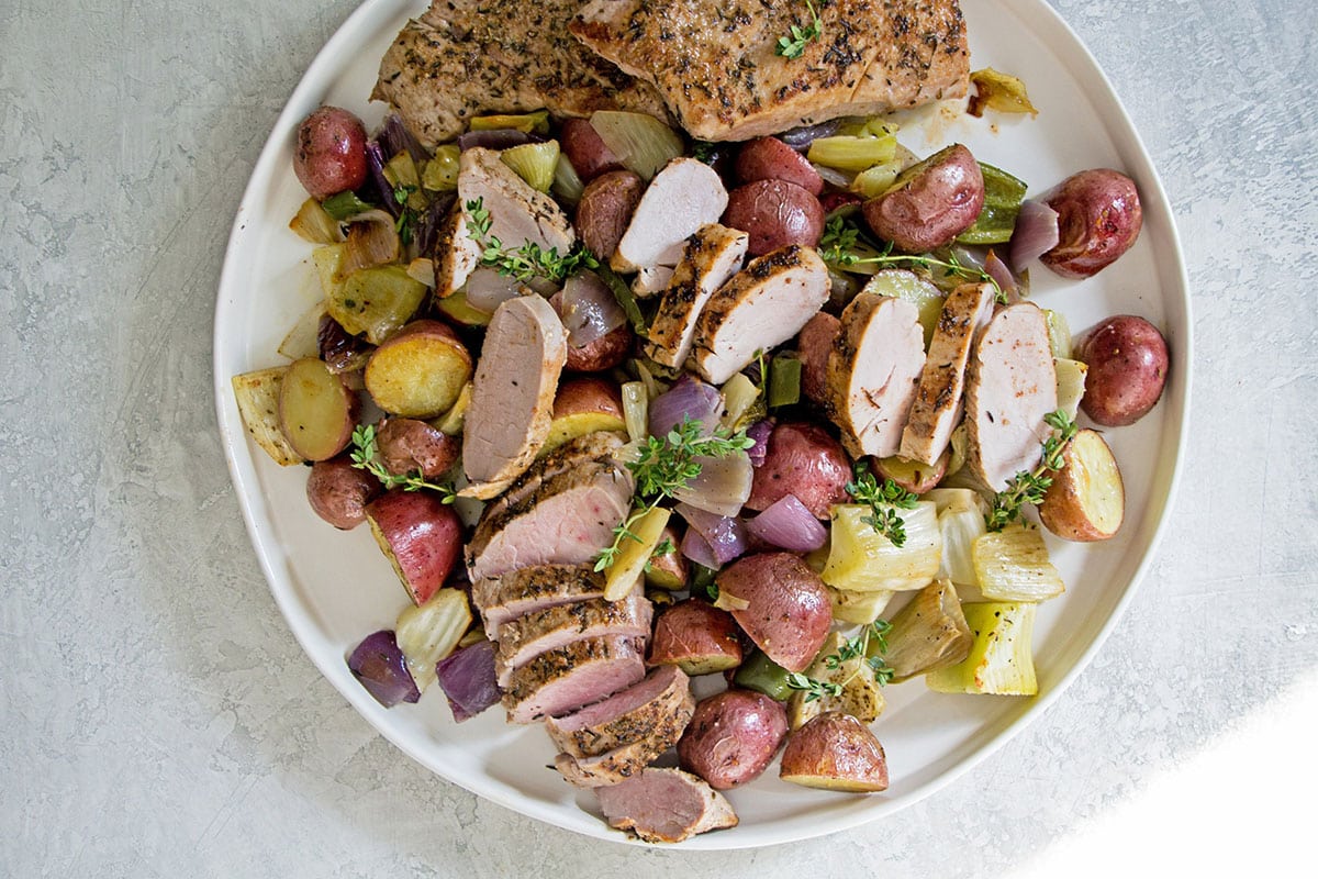Mediterranean-style pork tenderloin and roasted vegetables on large white plate.